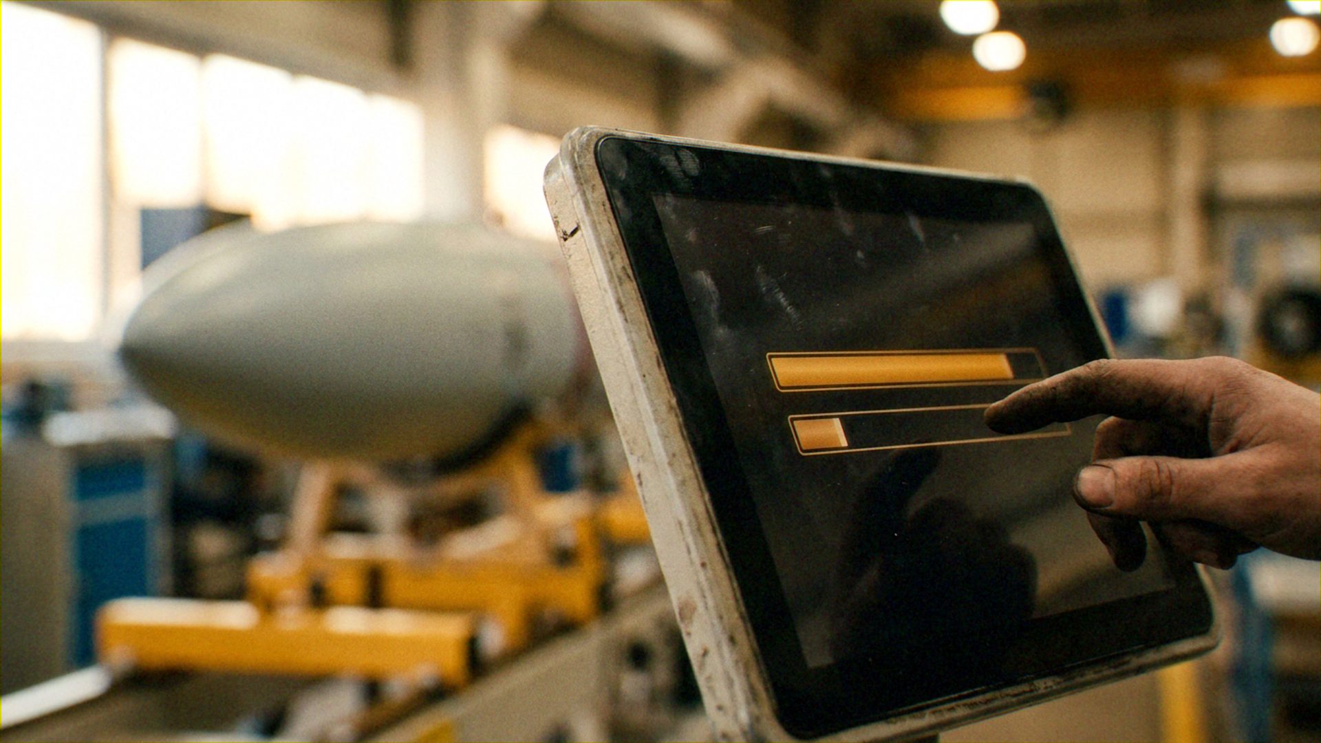 ['Manual technician/laborer', 'Ruggedized digital monitoring system', 'Physical aerospace component (fuselage or airframe)']. A technician is interacting with a digital interface to record data, verify completion, or monitor the assembly status of a physical hardware component..