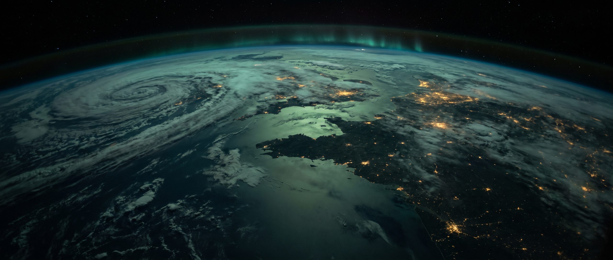 The same hemisphere from orbit, the storms still turning but the whole visible face of it lying quiet under a steady emerald airglow, city light warm and unbroken through the cloud.